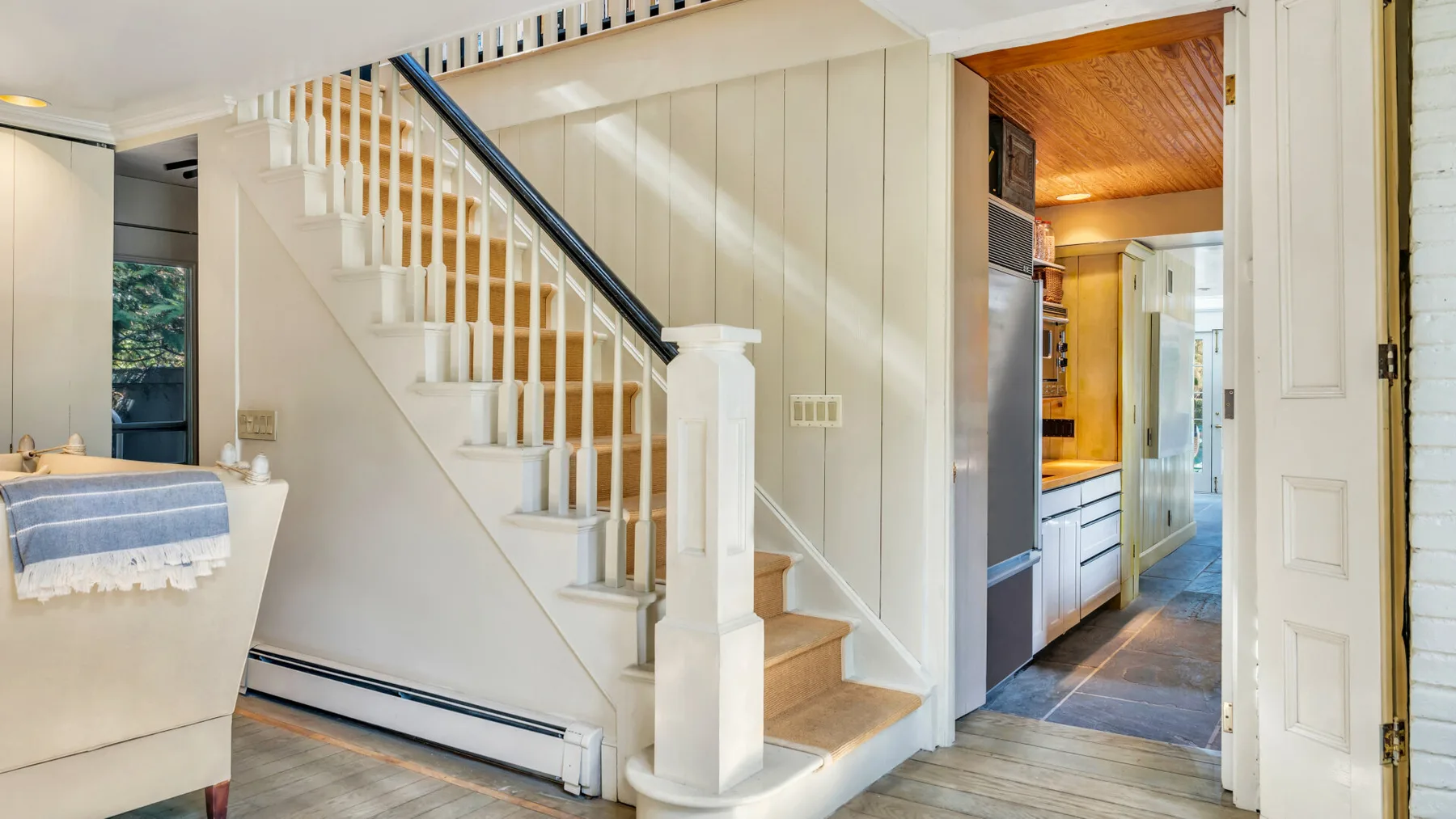 An interior hallway with a staircase beside an open doorway to a kitchen.
