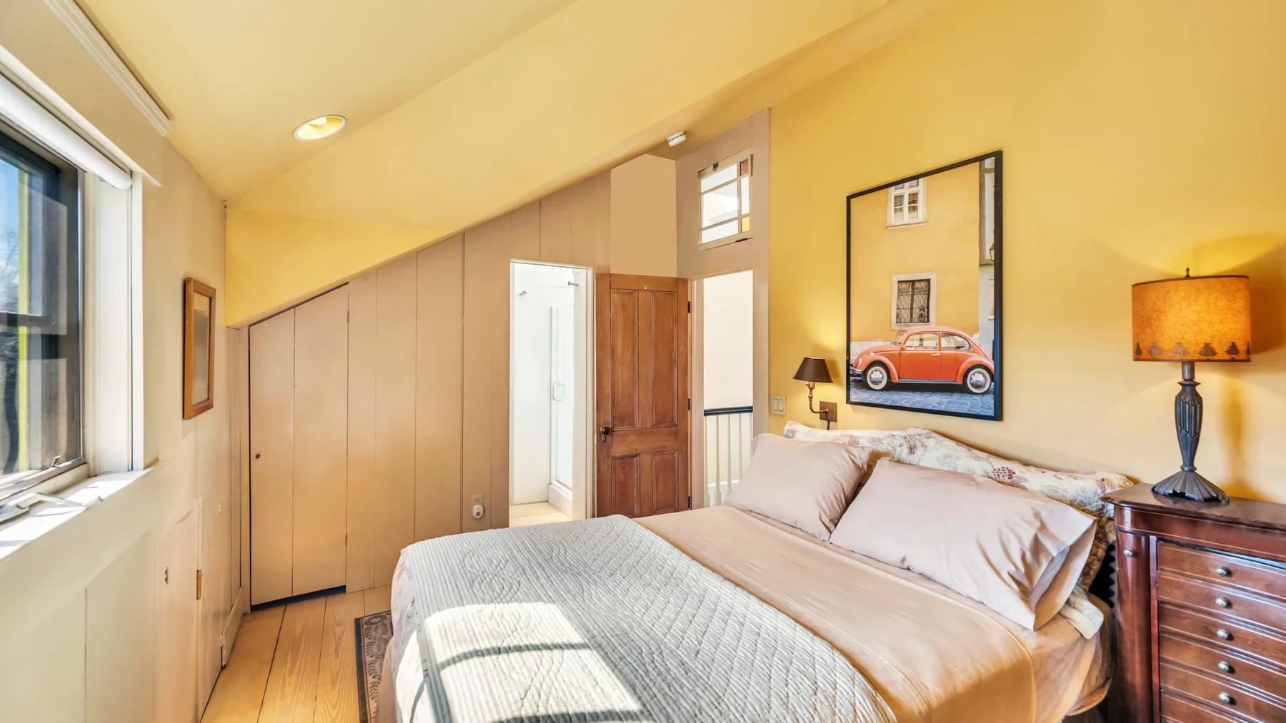 A bedroom with a bed, framed wall art, and a window.