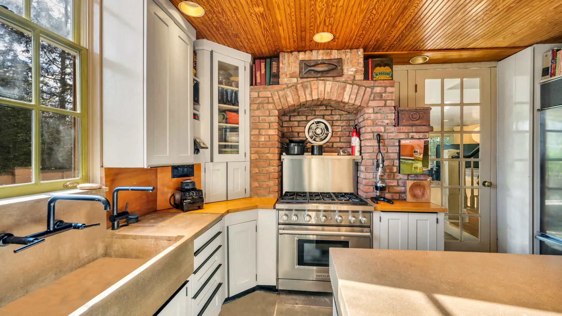 A bright kitchen with a brick cooking alcove and large windows.