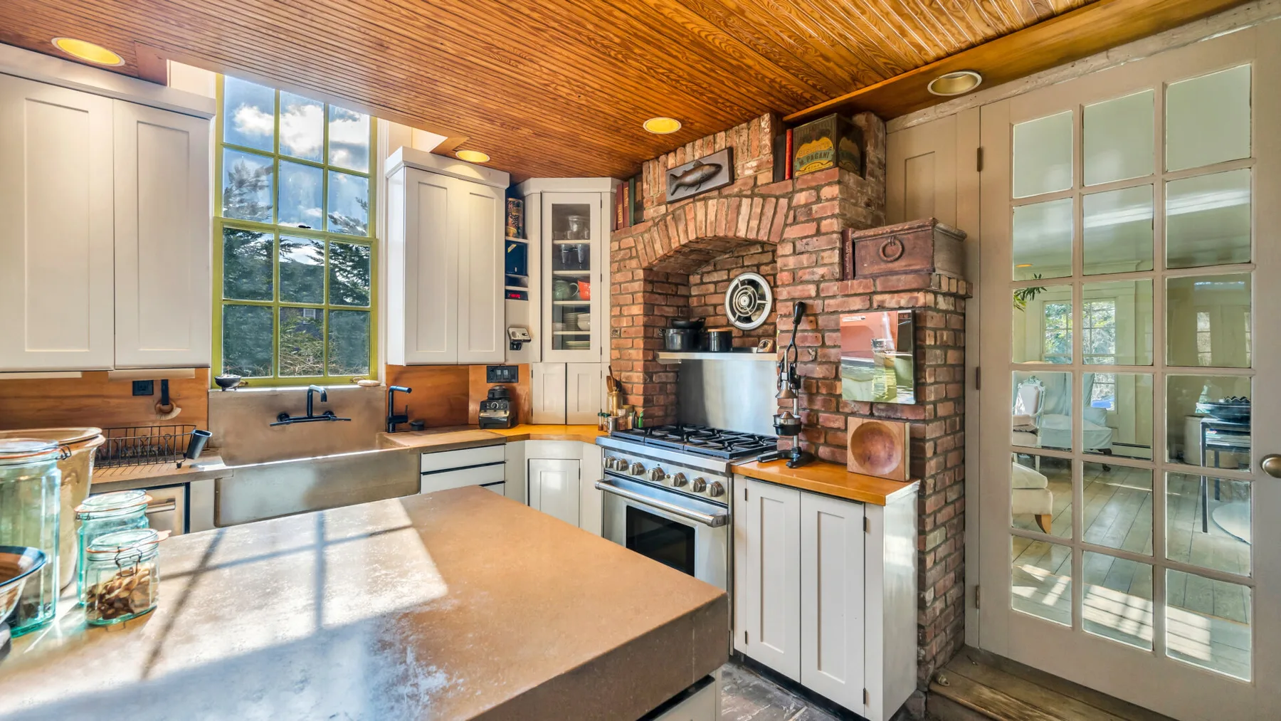 A bright kitchen with a large island, windows, and a brick cooking alcove.