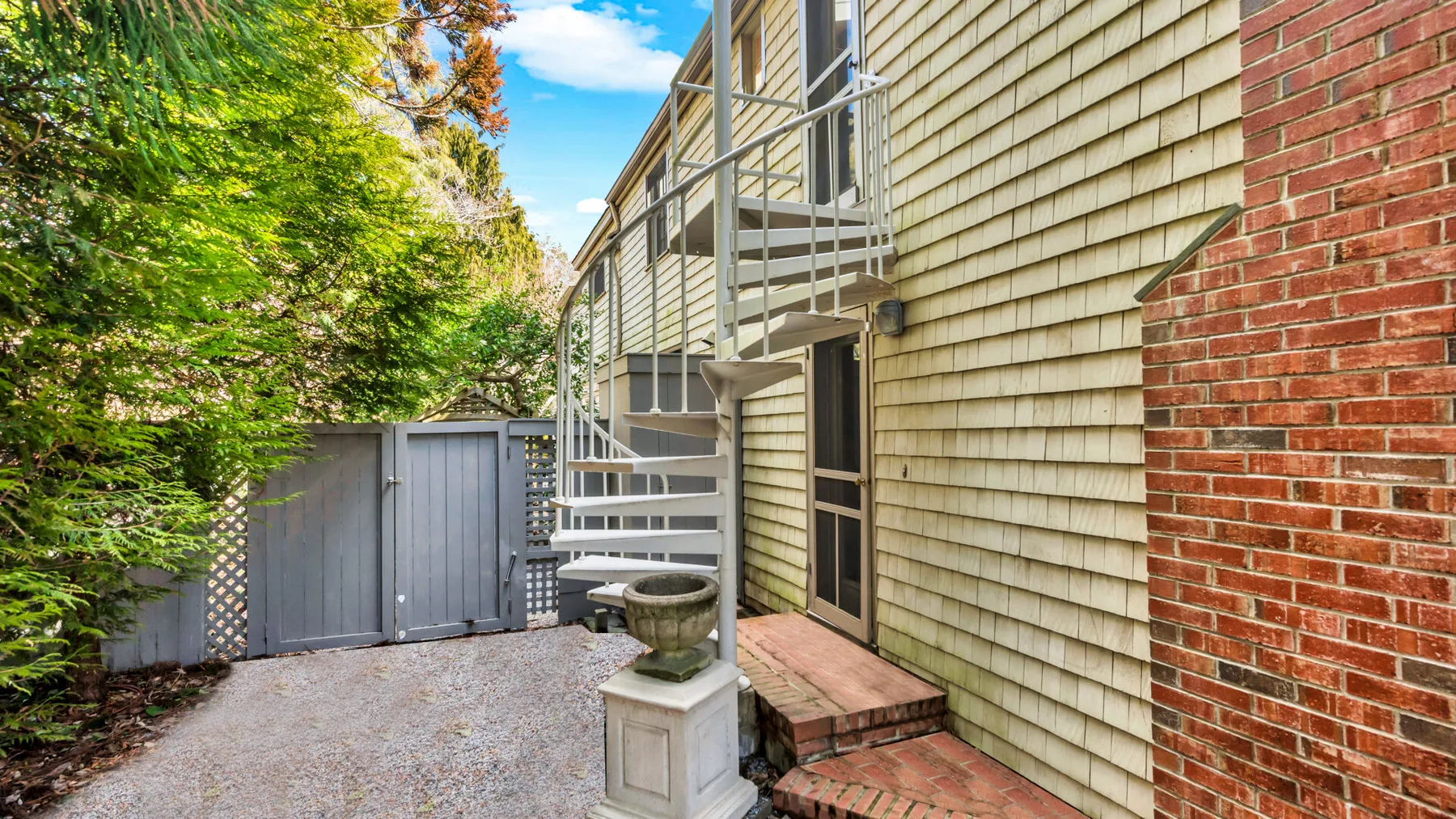 An exterior walkway beside a shingled building, with stairs and a gravel path.