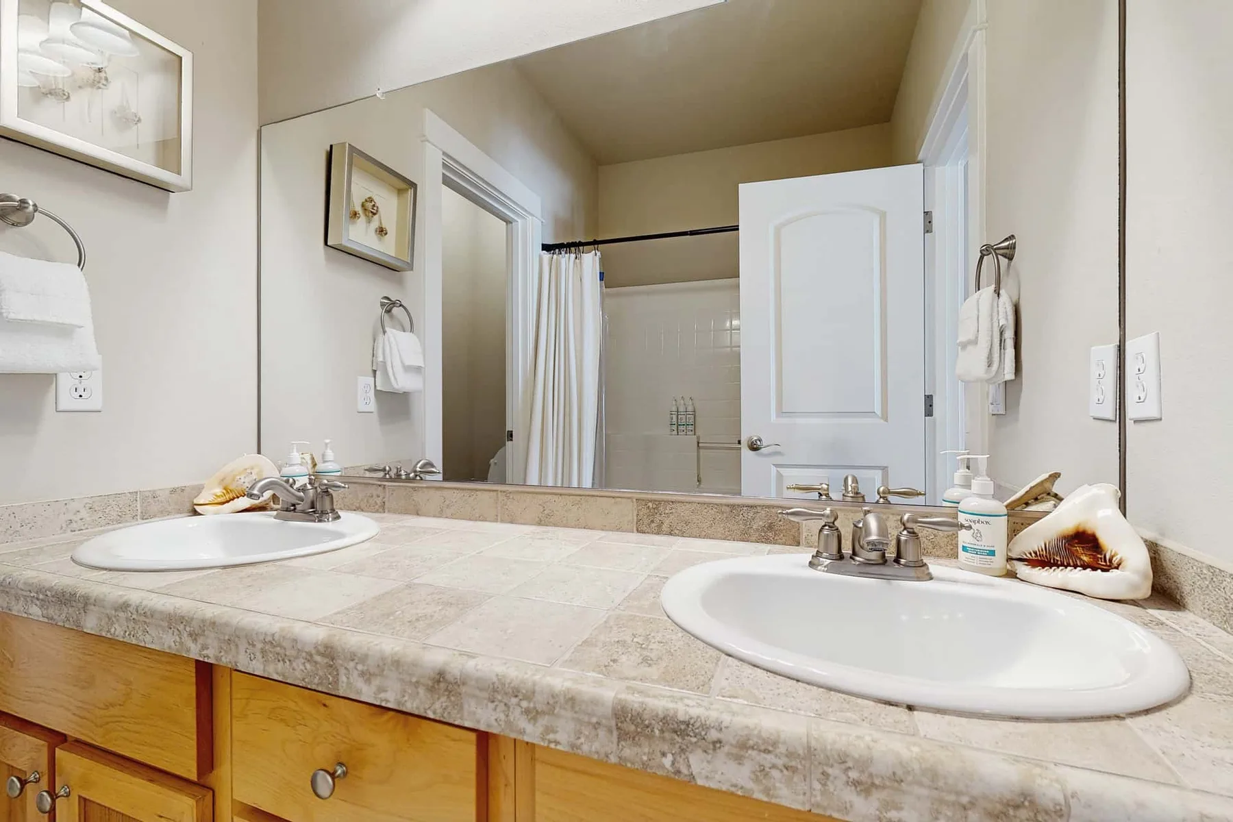 A bathroom vanity with two sinks faces a mirror beside an open shower area.