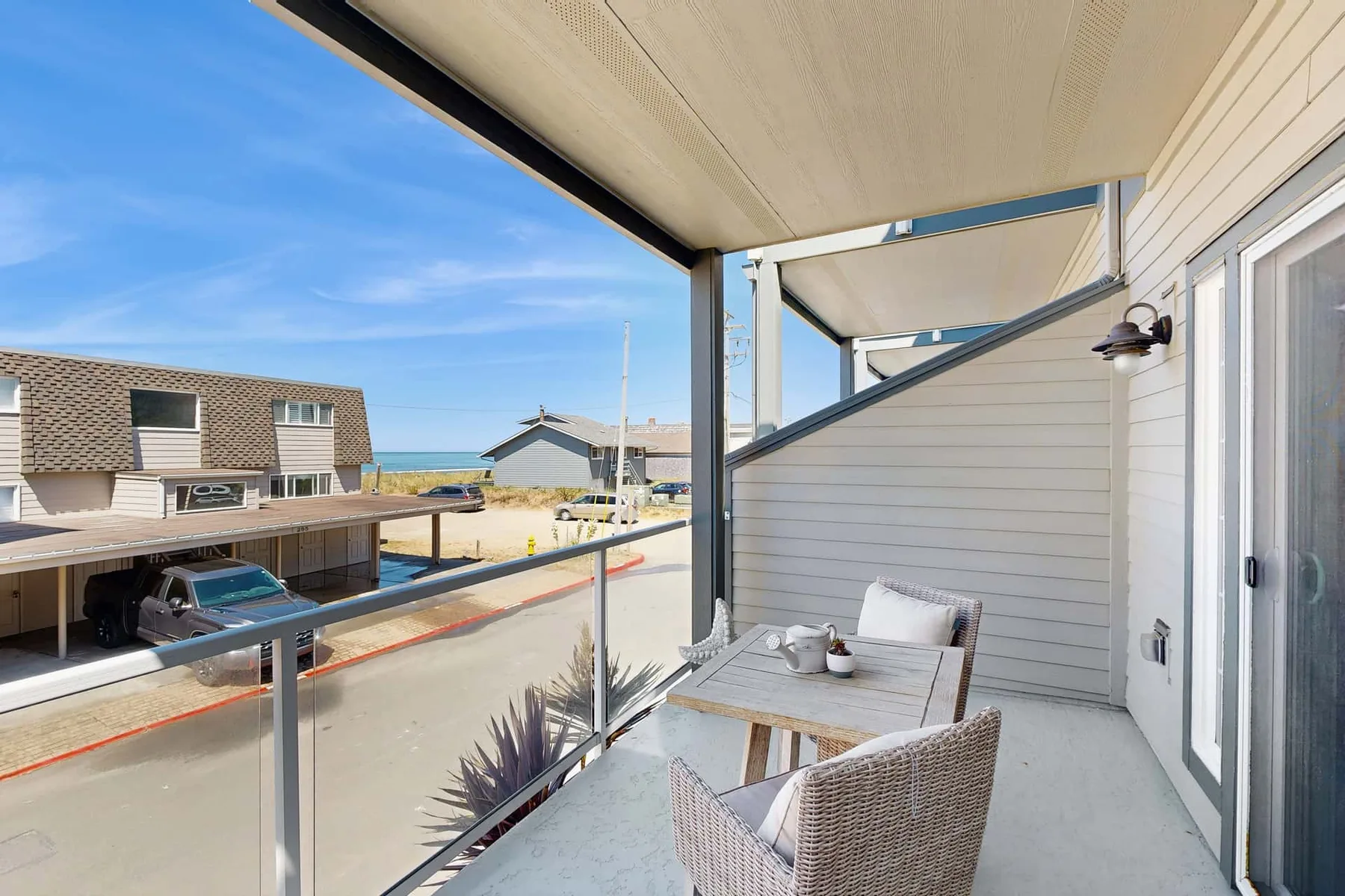 A covered balcony with outdoor seating overlooks nearby buildings and the ocean.