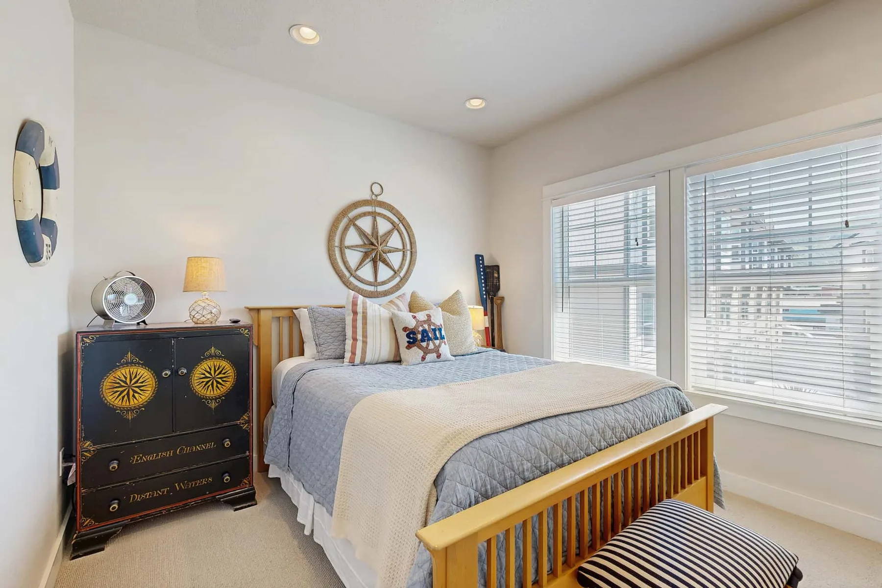 A bright bedroom with a bed beneath a nautical wall decoration.