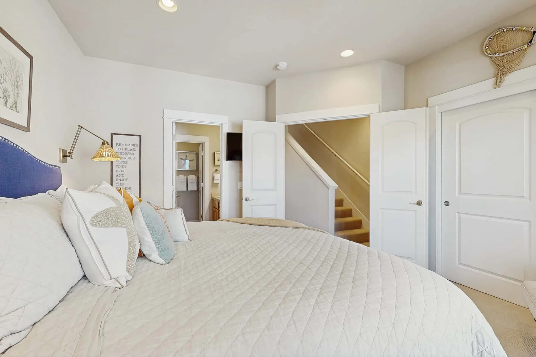 A bedroom with a large bed and a staircase visible through the open doorway.
