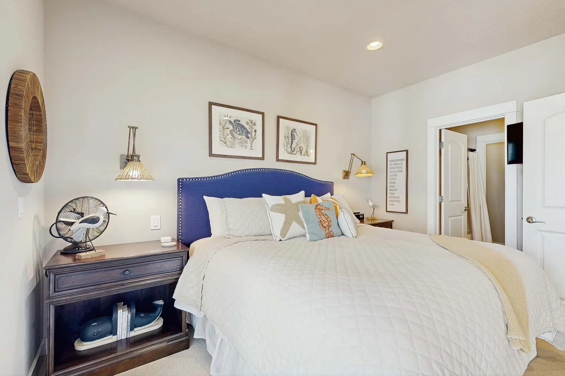 A bedroom with a neatly made bed, blue headboard, and framed artwork.