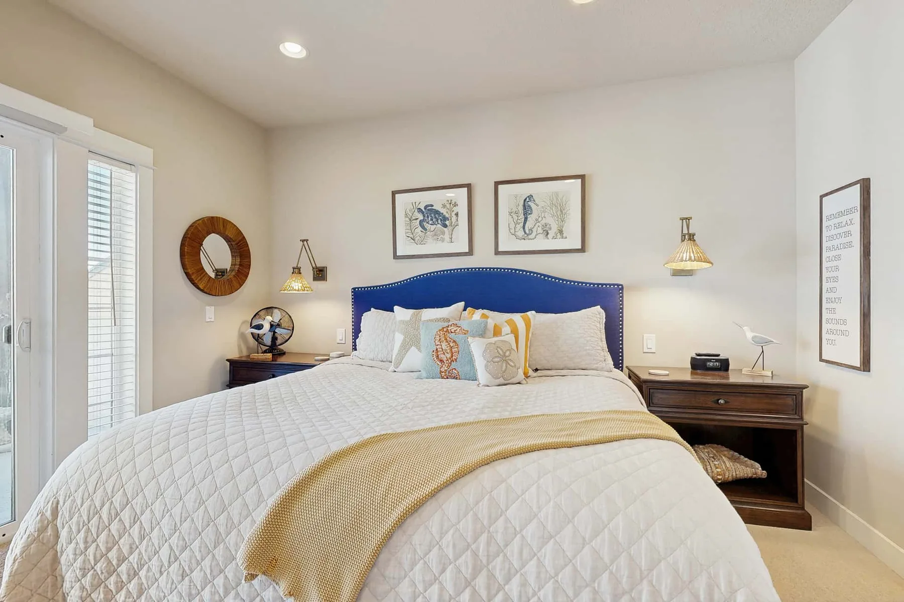 A bright bedroom features a large bed with white bedding and a blue headboard.
