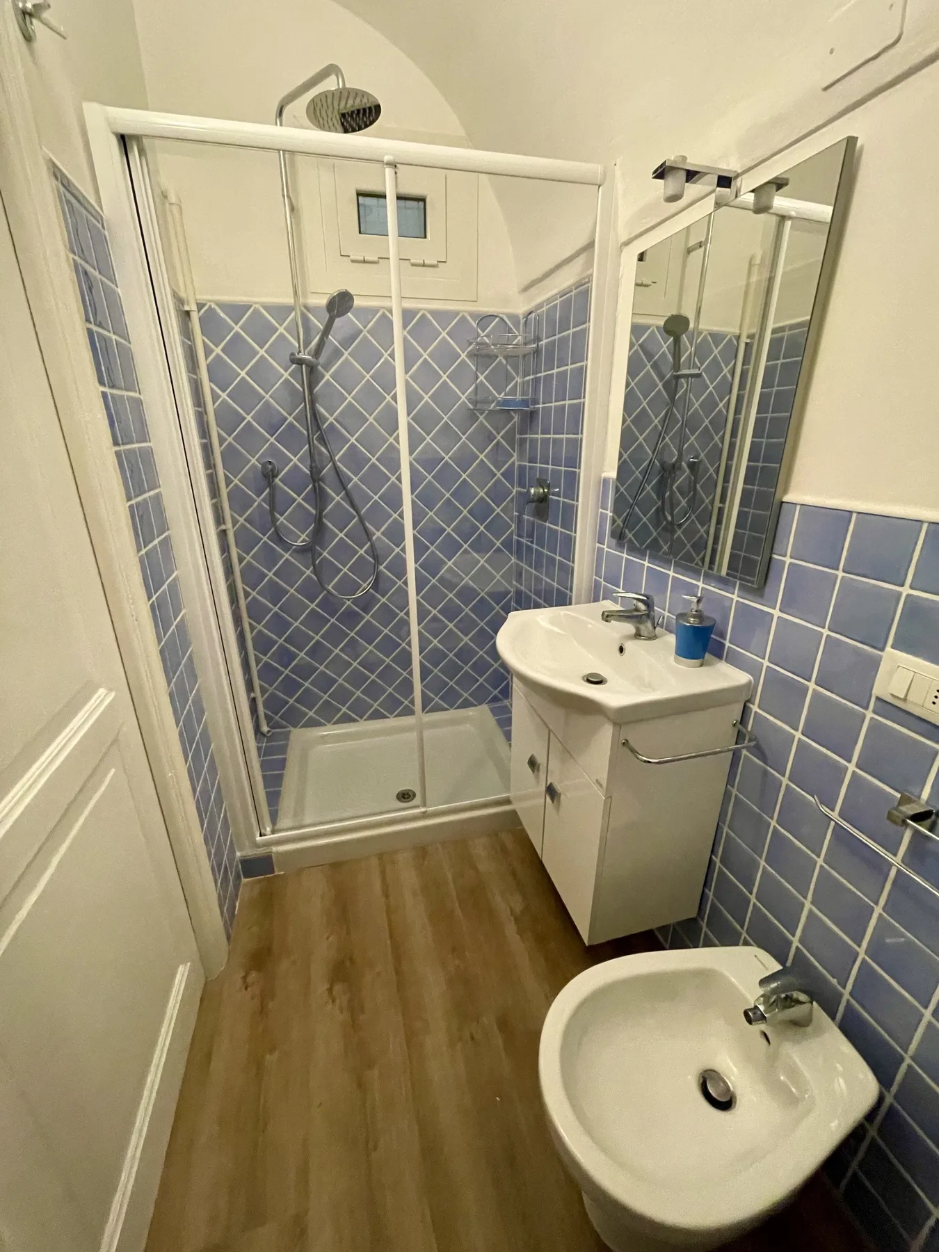 A tiled bathroom with a glass shower, sink, and bidet.