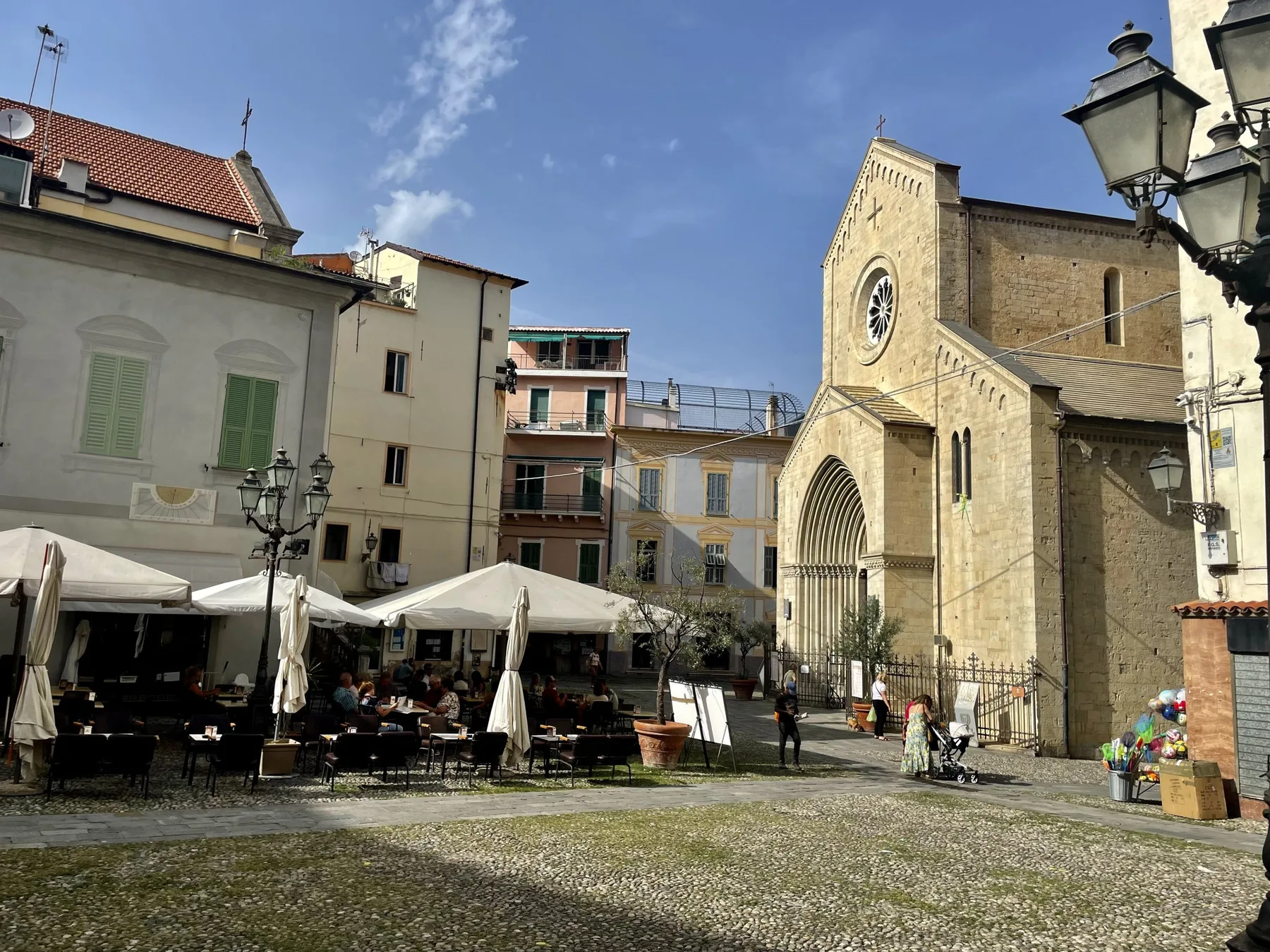 A sunlit town square with outdoor café seating beside a large stone church.