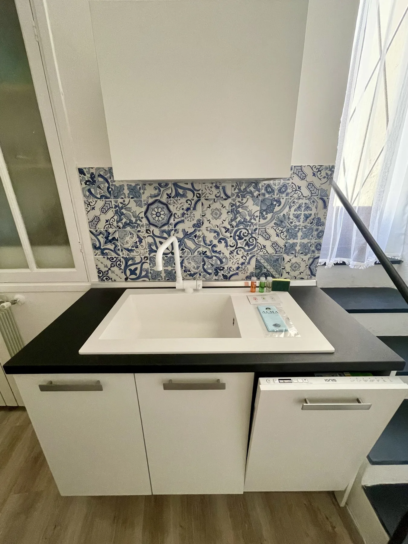 A bathroom vanity with a rectangular sink, patterned tile backsplash, and window.