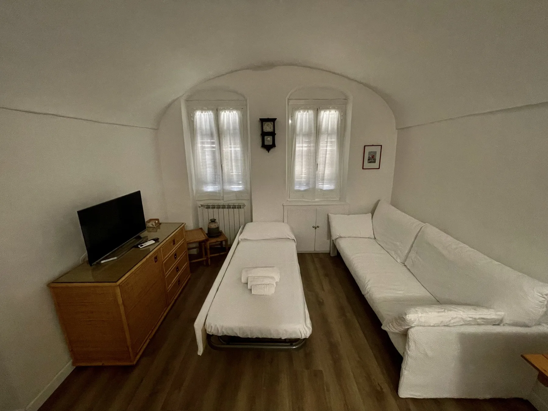 A narrow bedroom with a single bed, a long sofa, and a television.
