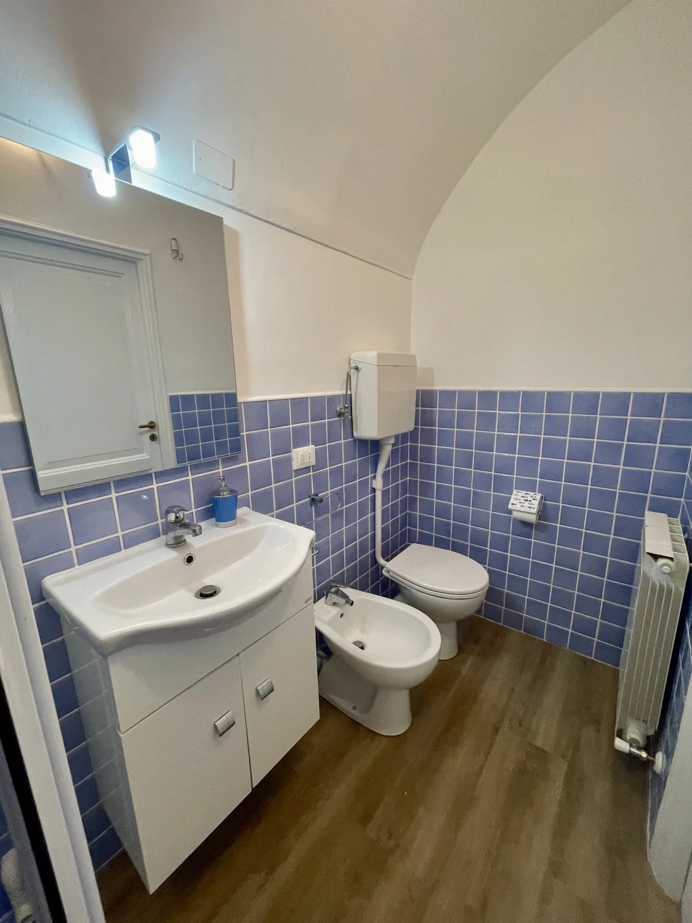 A bathroom with a sink, toilet, bidet, and blue tiled walls.