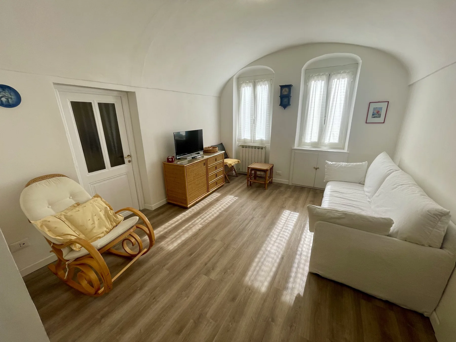 A bright living room with a white sofa, wooden cabinet, and rocking chair.