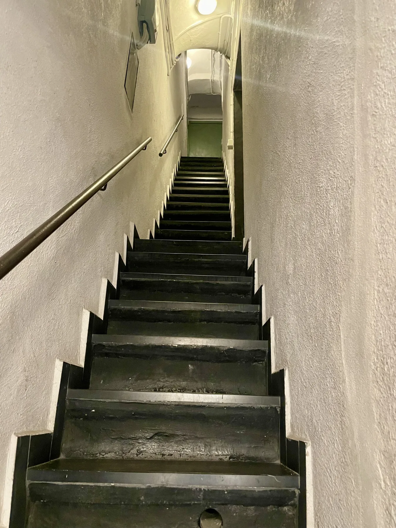 A narrow indoor staircase with dark steps and handrails along the walls.