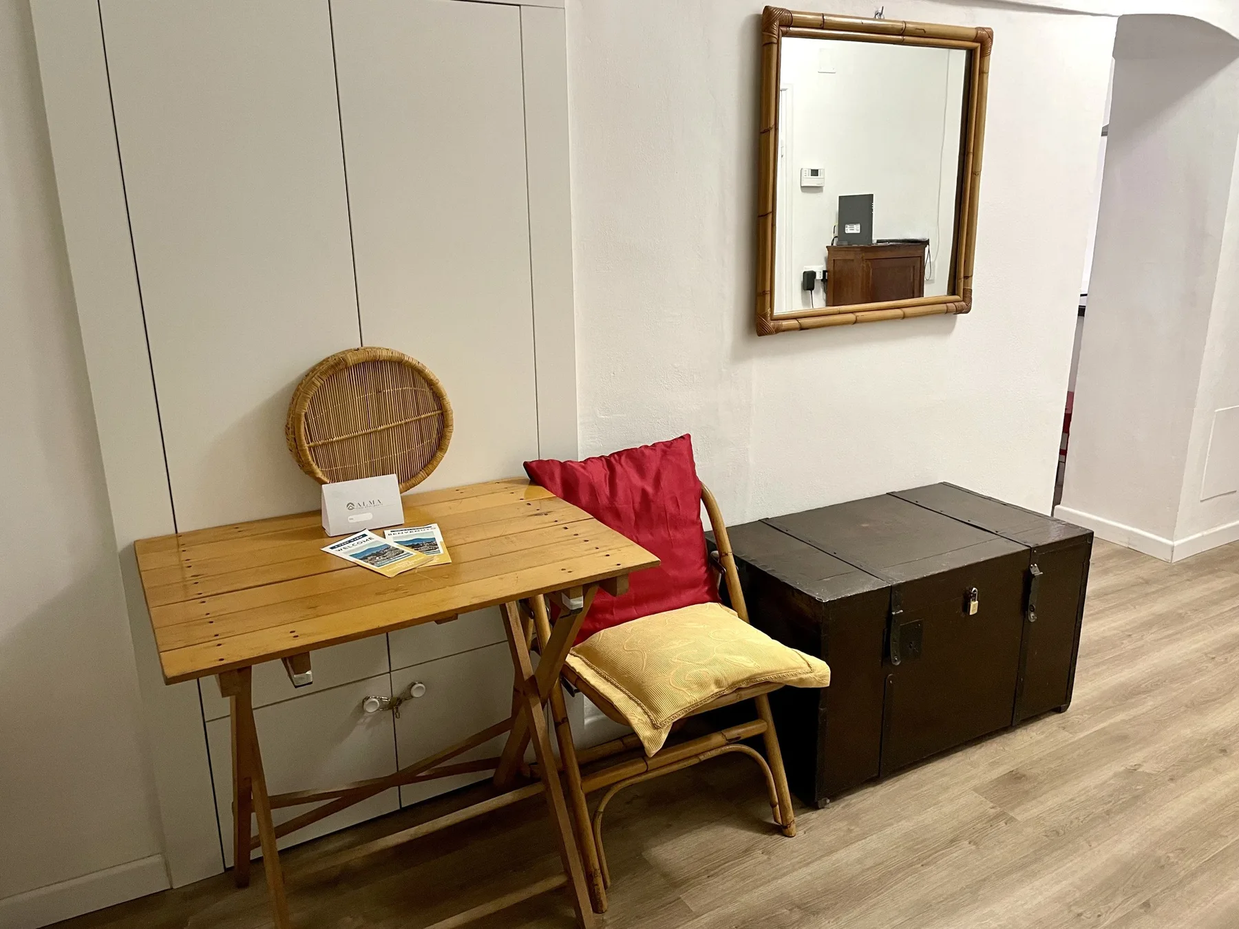 A small seating area features a wooden table, chair, and dark storage chest.
