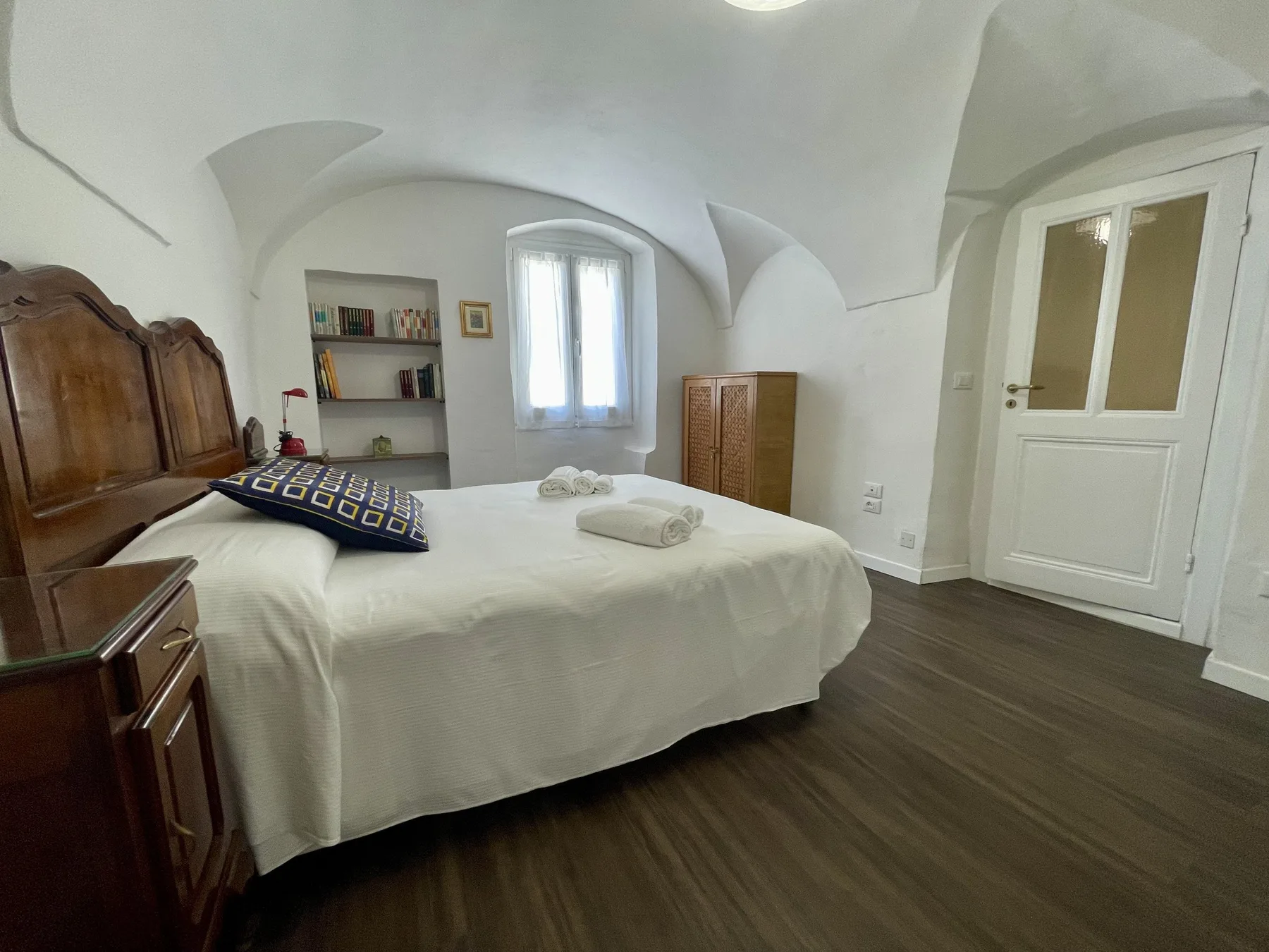 A bedroom with a white bed, wooden furnishings, and a small window.