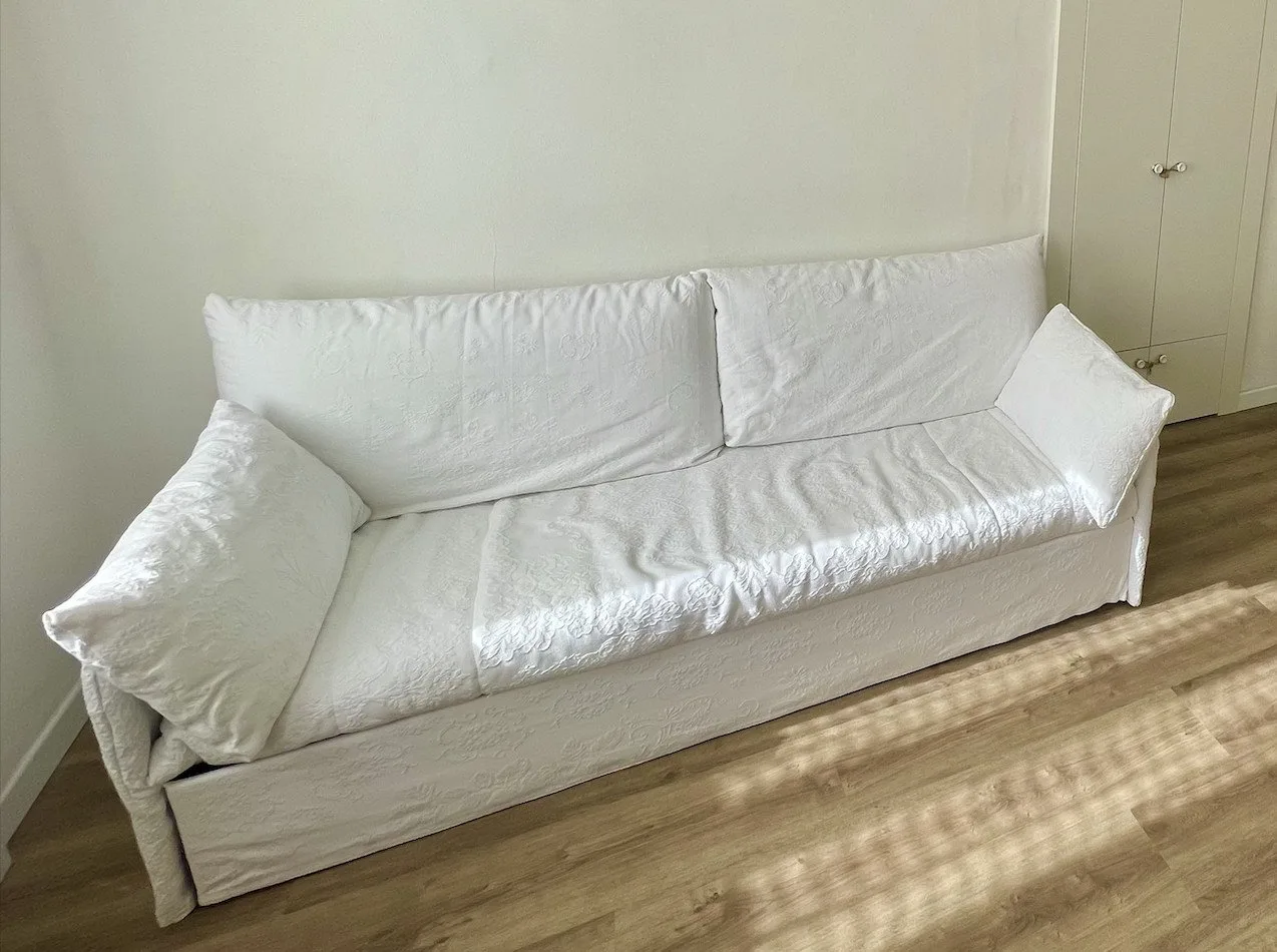 A white sofa sits against a plain wall above a wood floor.