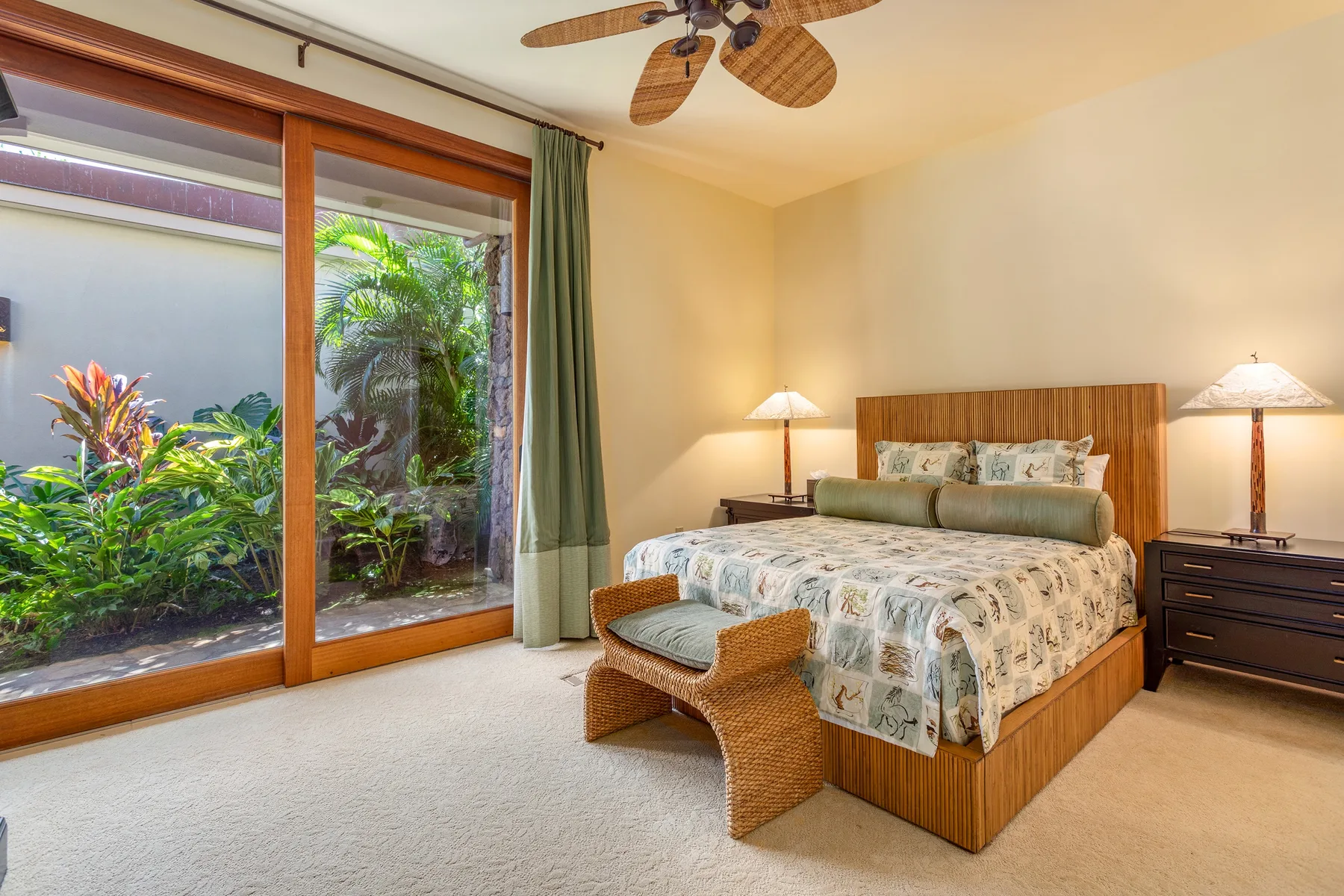 A bedroom with a wooden bed, patterned bedding, and sliding glass doors to greenery.
