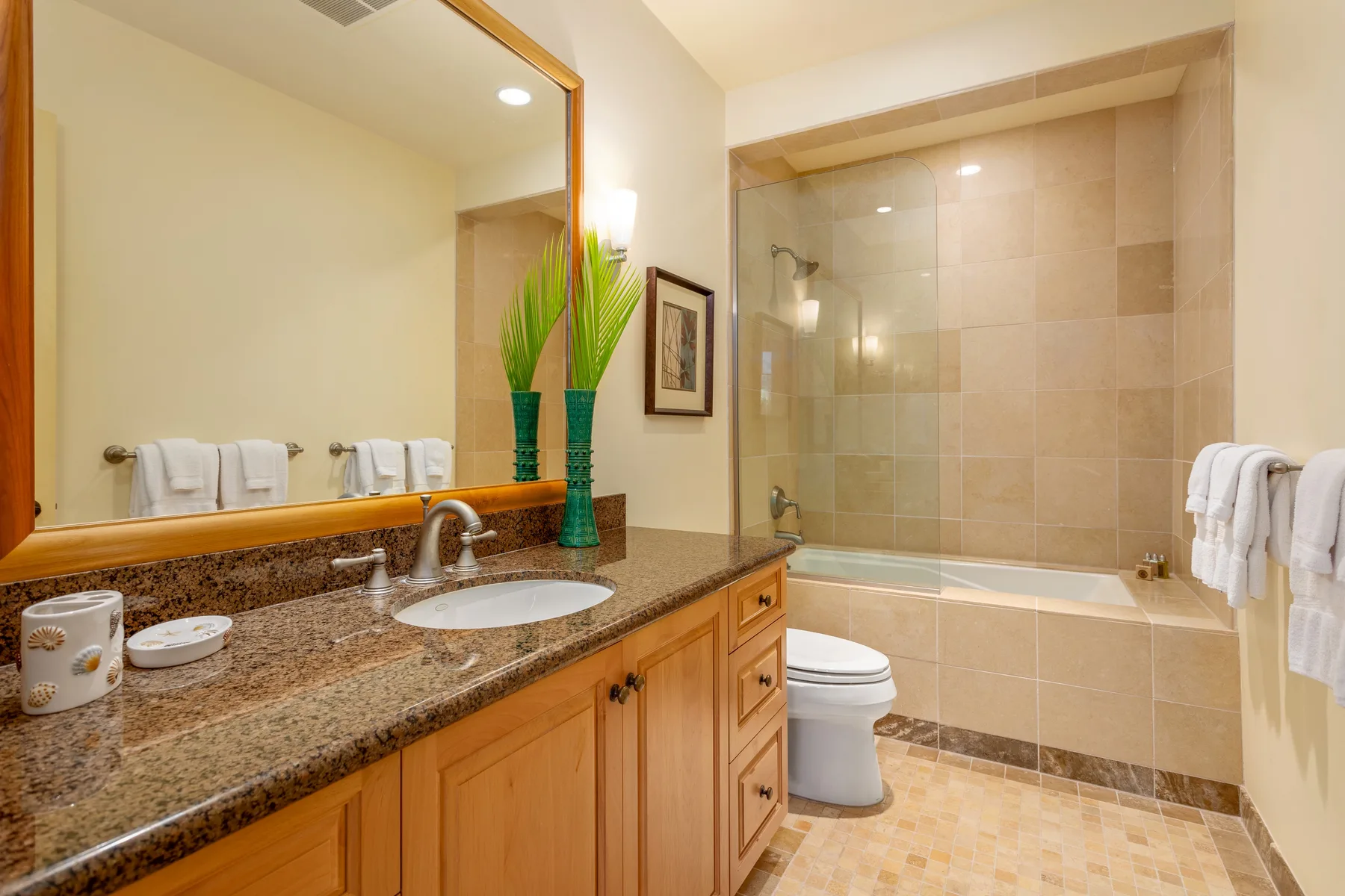 Bathroom with a long vanity, sink, toilet, and bathtub behind a glass panel.