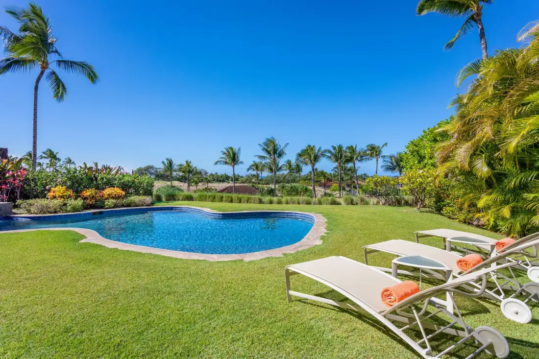 A landscaped outdoor pool area with lawn, palm trees, and lounge seating.