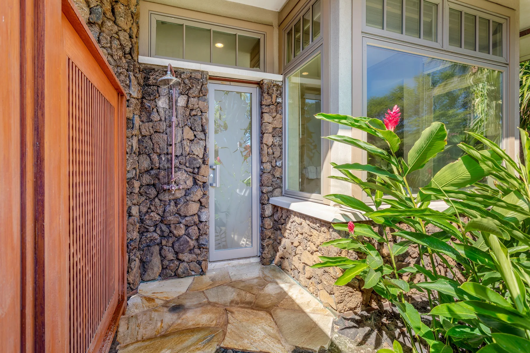 A glass shower area is set beside stone walls and a large window.