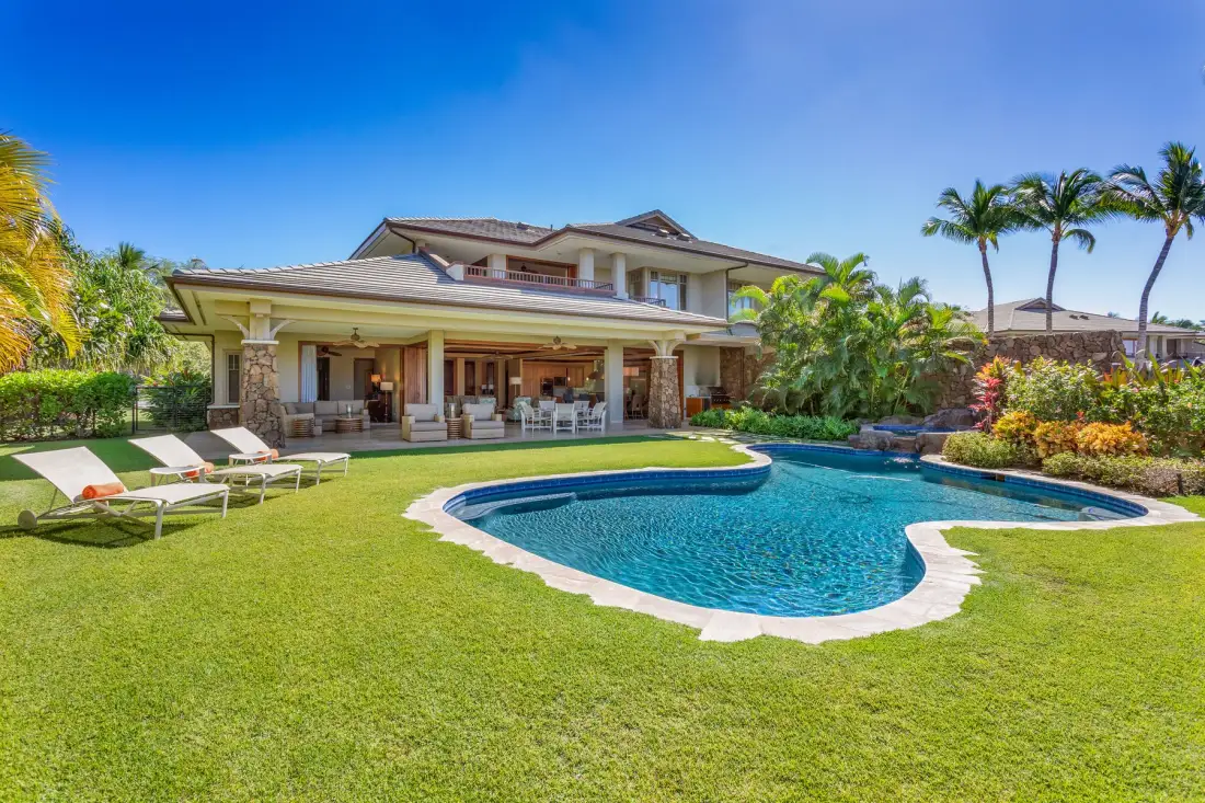 A landscaped backyard with a curved swimming pool and a covered patio.