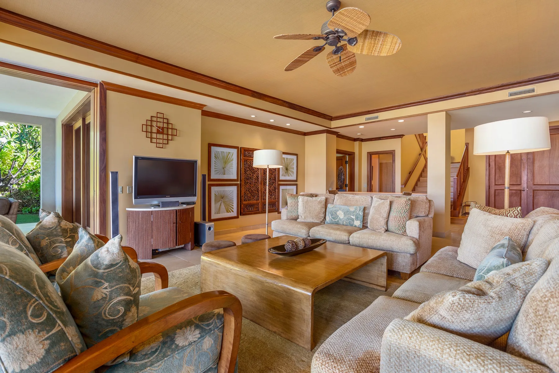 A bright living room with cushioned seating, a wooden coffee table, and a television.