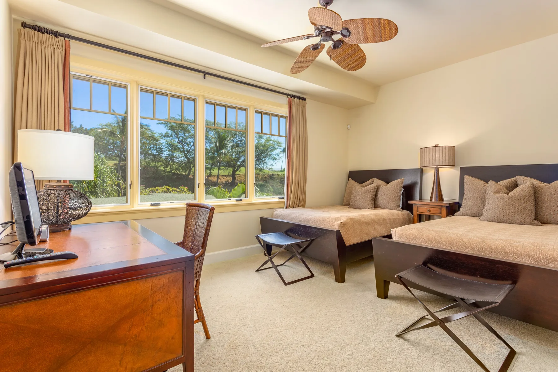 A bright bedroom with two beds, a desk, and large windows.