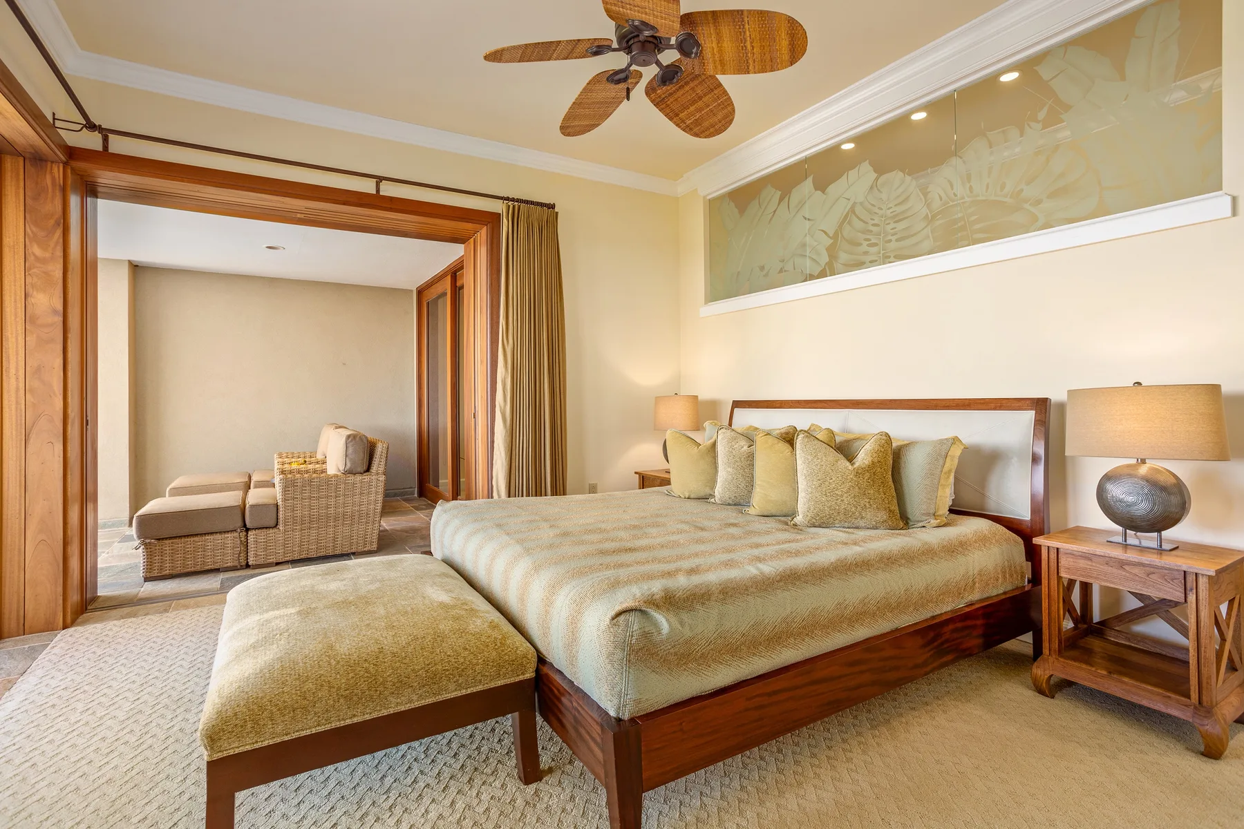 A bedroom with a large bed, cushioned bench, and ceiling fan.