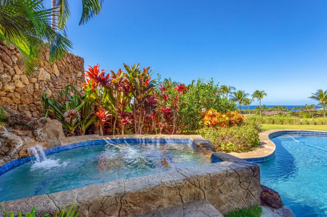 Outdoor swimming pool with a bubbling spa beside tropical plants and ocean views.
