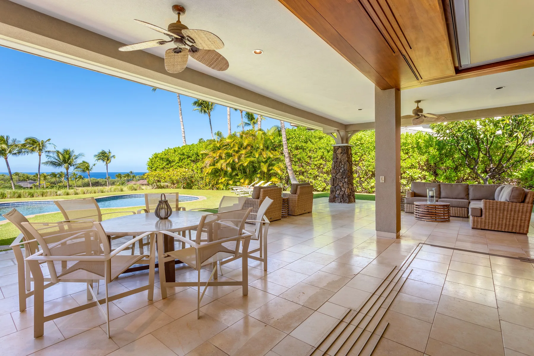 A covered outdoor dining and lounge area overlooks a pool and lush greenery.