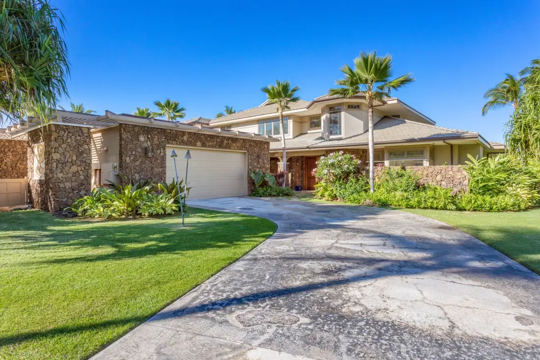 A house with a curved driveway, green lawn, and palm trees.