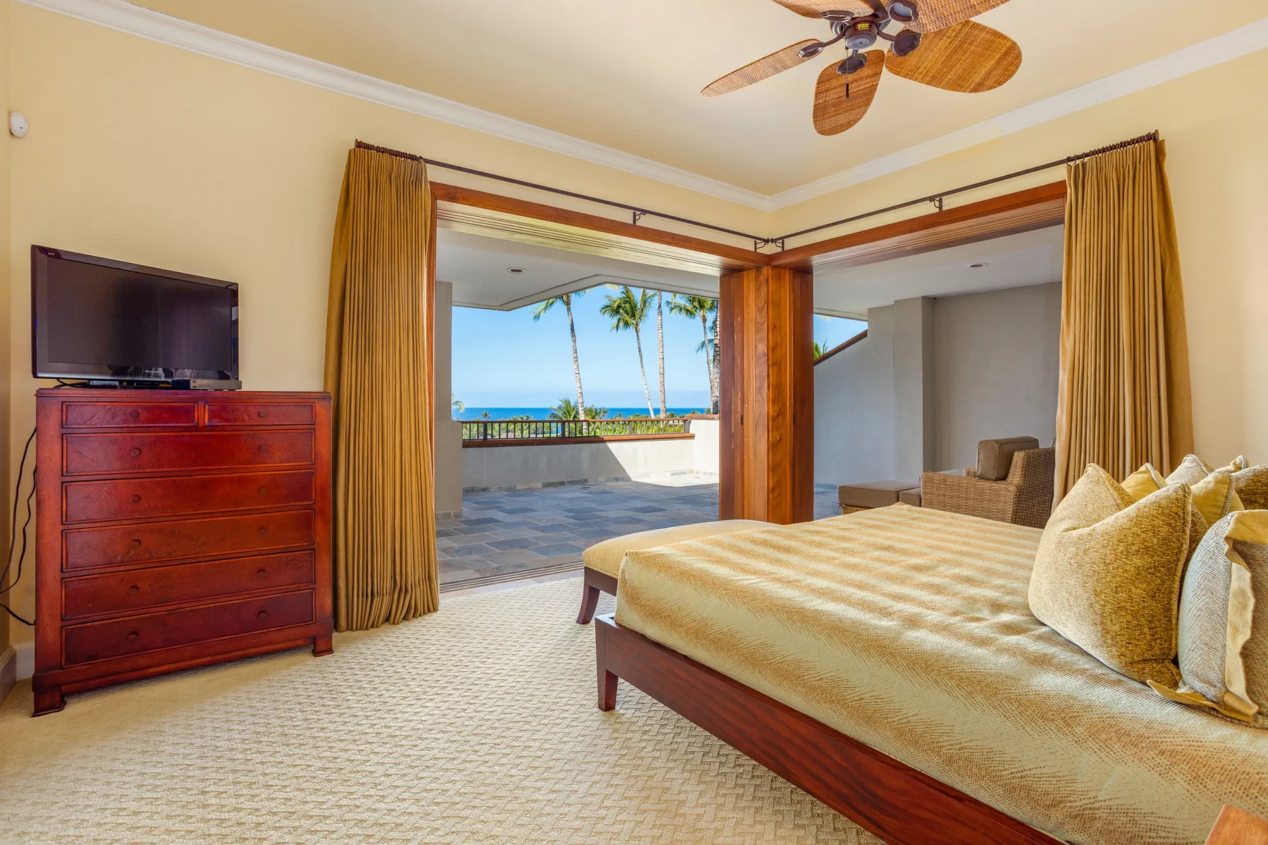 A bedroom opens onto a terrace with ocean views and palm trees.