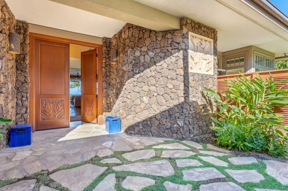 A stone-clad entrance with an open wooden door and a paved path.