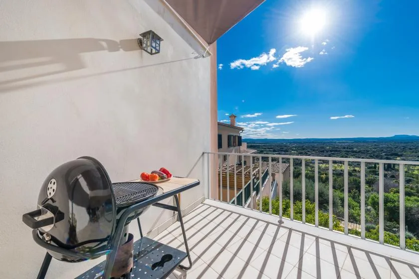 A sunny balcony with a barbecue grill and views over a green landscape.