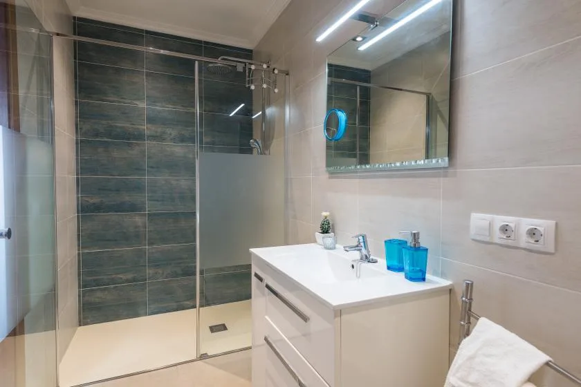 A tiled bathroom with a glass shower, sink, and wall mirror.