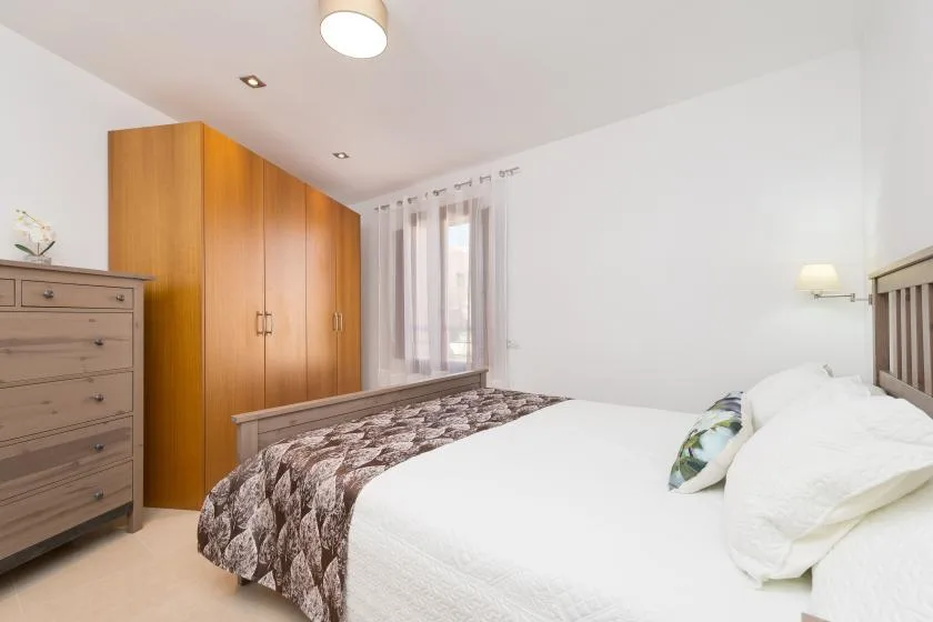 A bright bedroom with a bed, wooden wardrobe, and curtains over the window.