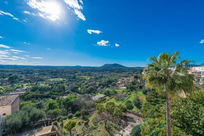 A sunny landscape view overlooks green countryside, scattered homes, and a distant hill.