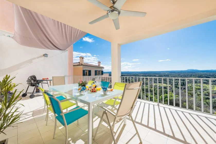 A covered balcony dining area with a glass table and views of the landscape.