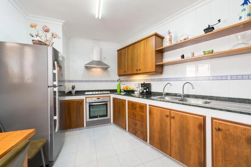 A bright kitchen with wooden cabinets, a refrigerator, and a double sink.