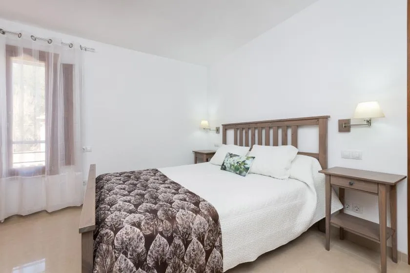 A bright bedroom with a bed dressed in white linens and a patterned blanket.