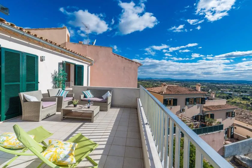 A tiled terrace with outdoor seating overlooks nearby buildings and a broad landscape.
