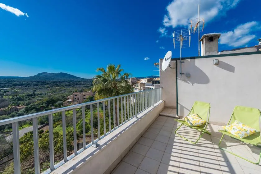A sunny rooftop terrace overlooks a green valley, with two lounge chairs beside the railing.