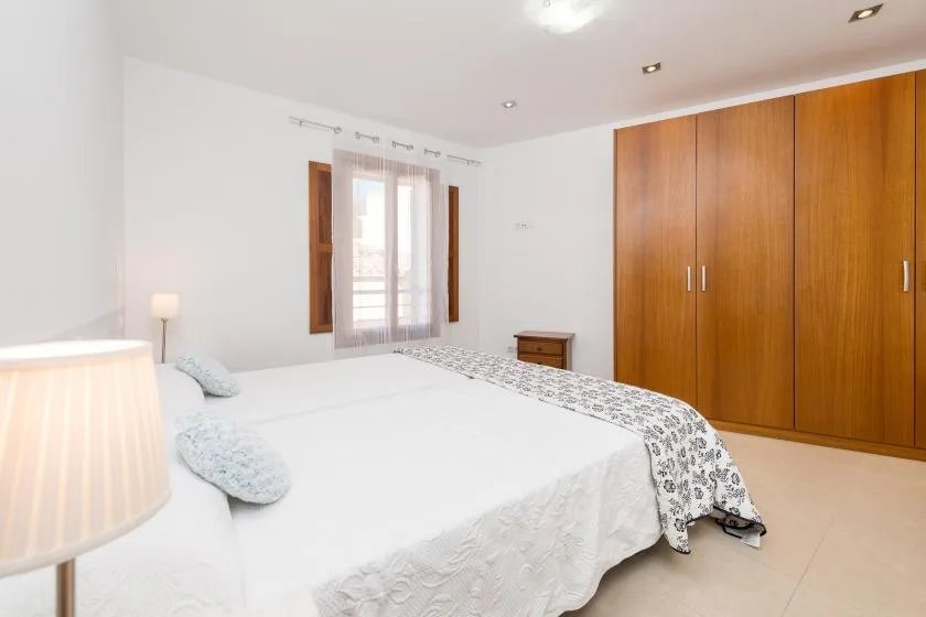 A bright bedroom with a bed, a window, and a large wooden wardrobe.