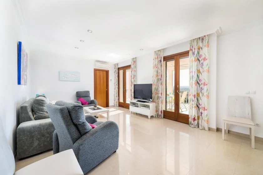A bright living room with seating, a television, and glass doors opening to a balcony.
