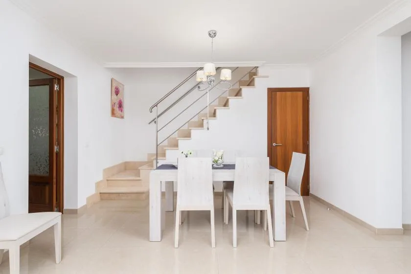 A bright dining area with a table and chairs beneath a staircase.