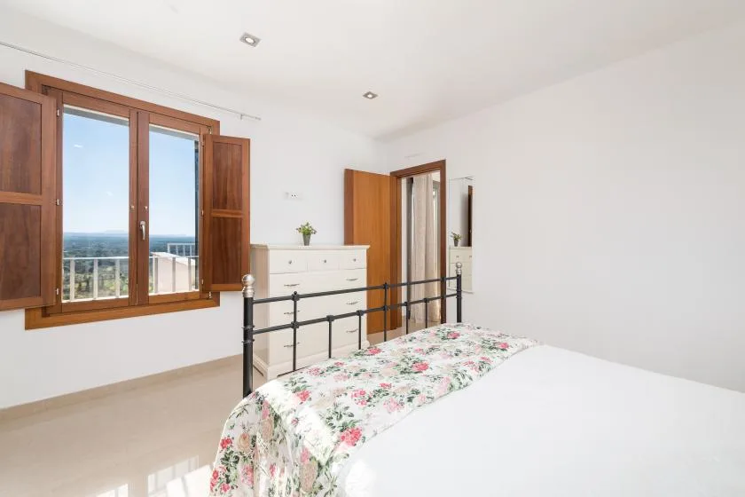 A bright bedroom with a floral bedspread and wooden-framed windows.