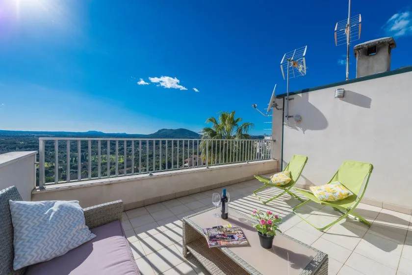 A sunny rooftop terrace has outdoor seating and a wide view of the surrounding landscape.