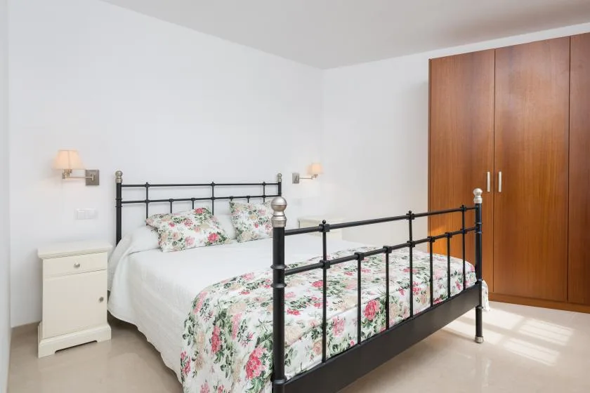 A bedroom with a metal bed frame, floral bedding, and a wooden wardrobe.