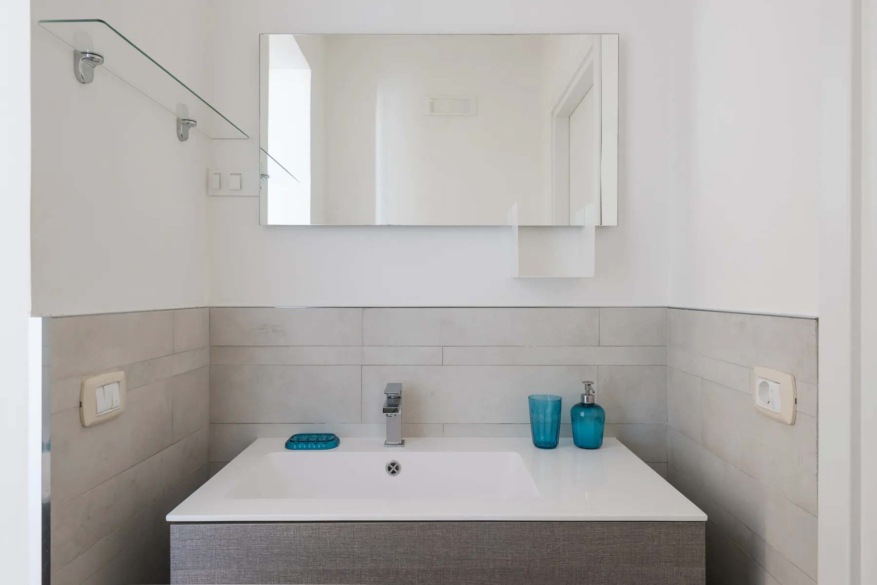 Un lavabo de baño con espejo de pared y paredes revestidas de azulejos.